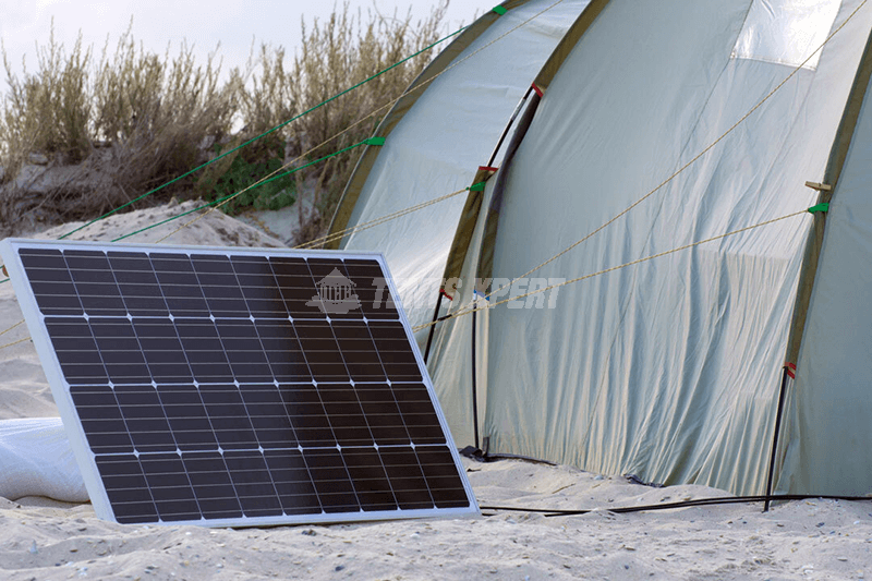 a solar panel placed on the sandy ground next to a large tent